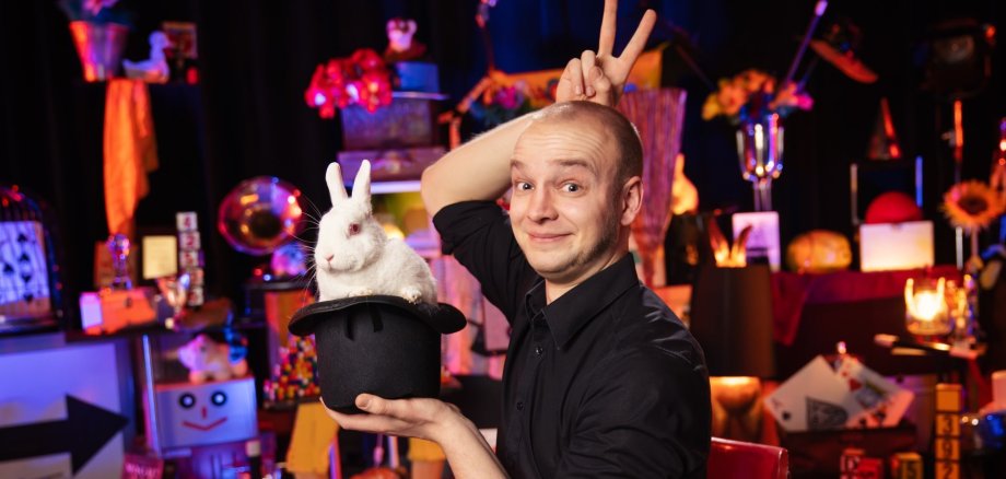 La photo montre le magicien Jakob Mathias avec un chapeau de magicien dans lequel se trouve un lapin blanc.