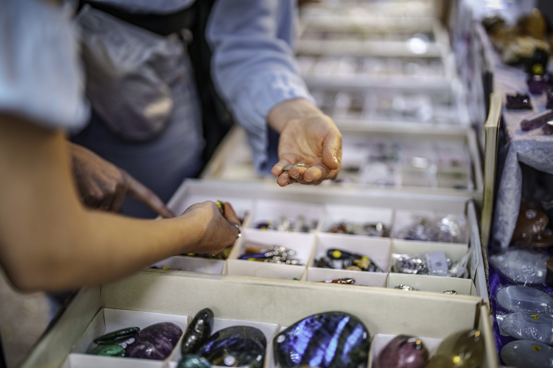 La photo montre une vue de l'étalage d'un magasin de pierres précieuses. On y voit les mains de deux clients saisissant des pierres.