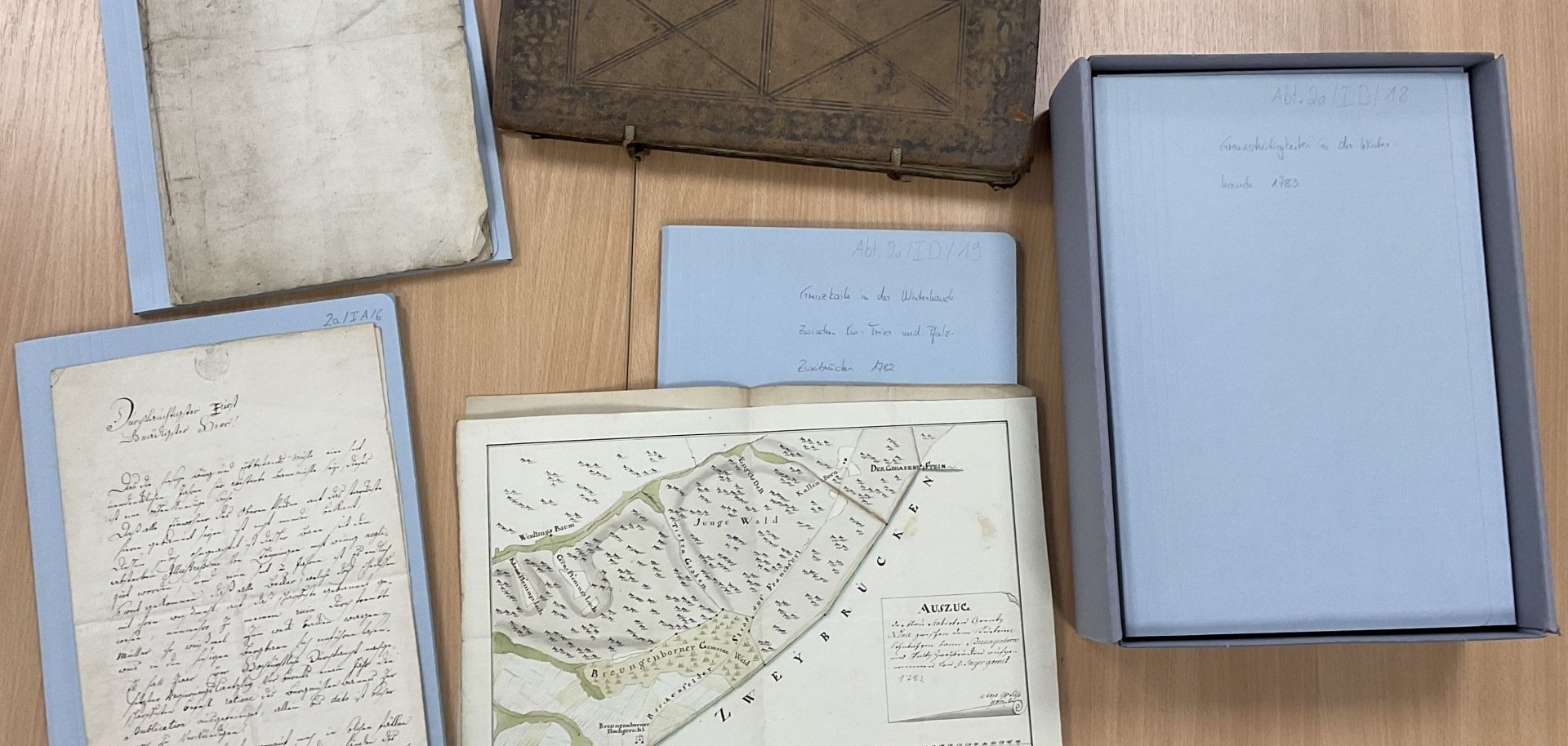 La photo montre quelques documents historiques ainsi que les nouveaux cartons et boîtes d'archives.