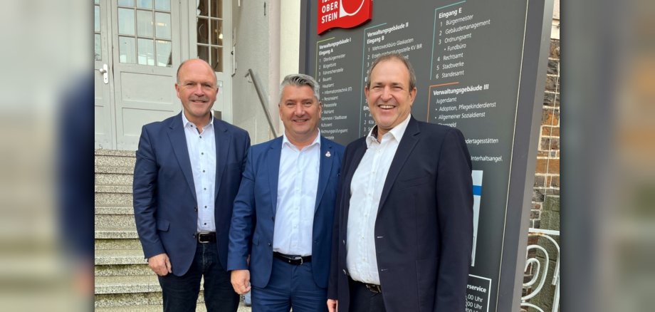 La photo montre les personnes mentionnées se tenant devant l'hôtel de ville au panneau indicateur de la municipalité.