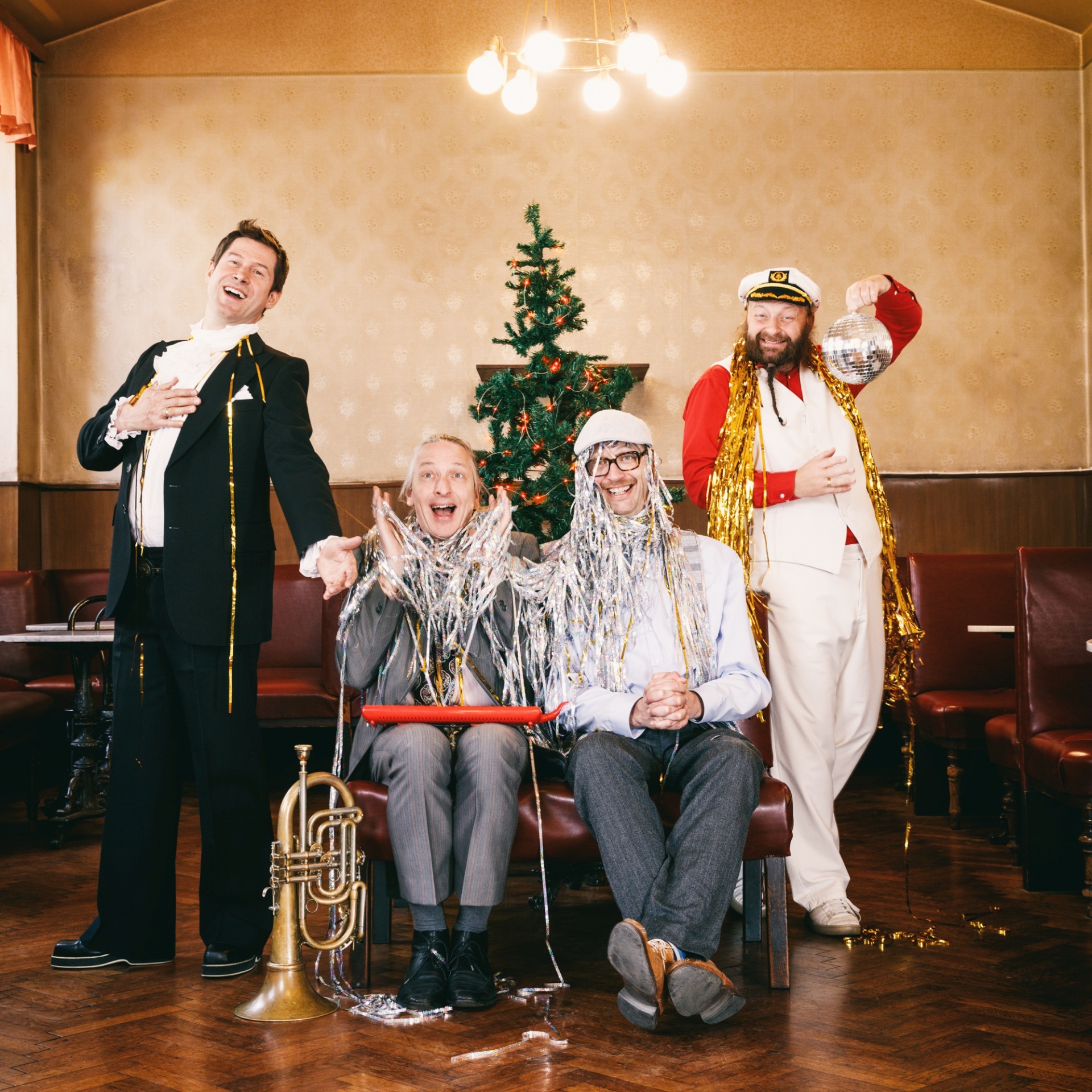 La photo montre les personnes susmentionnées debout ou assises en costume devant un arbre de Noël.