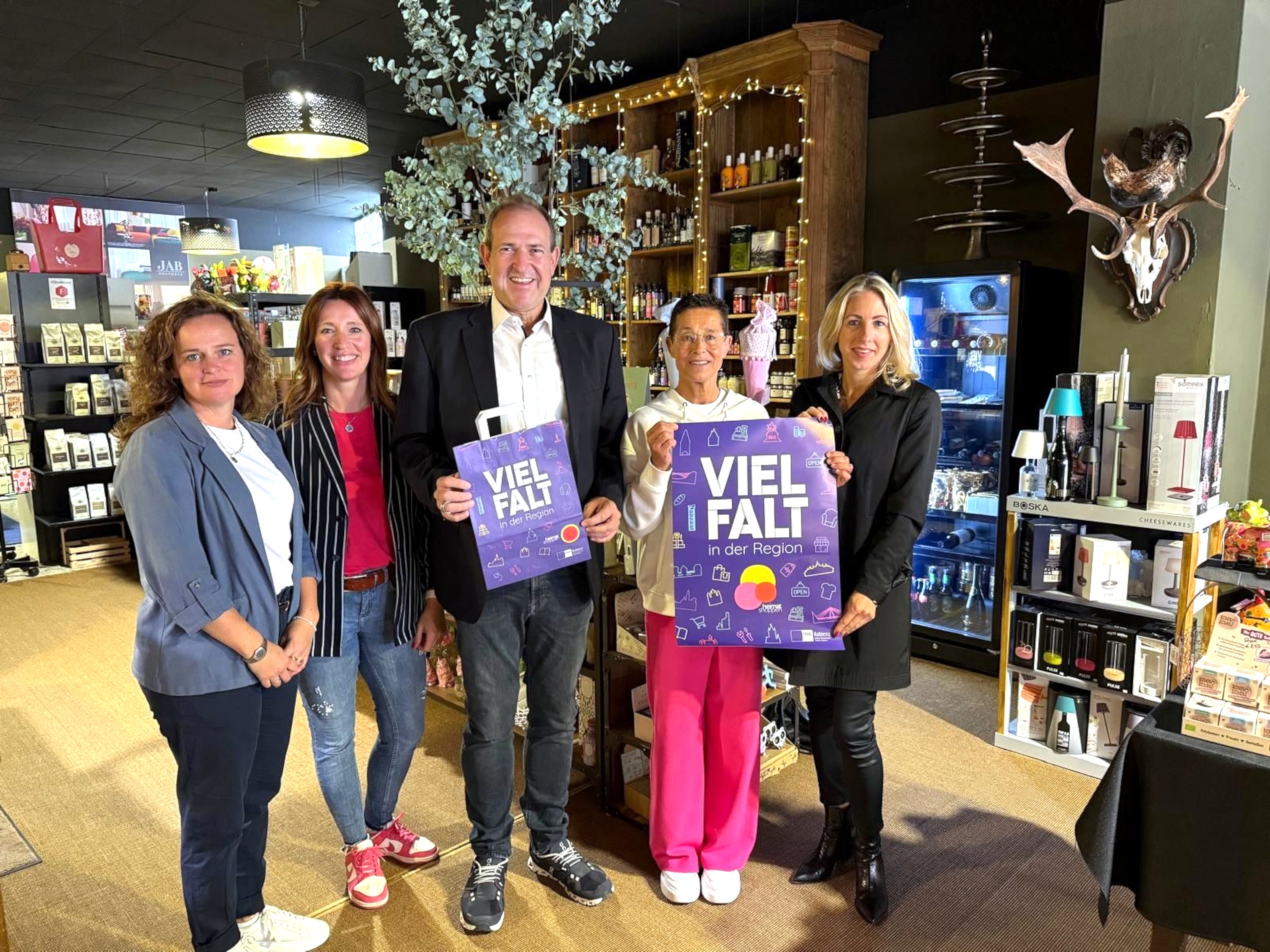 La photo montre les personnes mentionnées. Elles se tiennent côte à côte dans le magasin et regardent la caméra.
