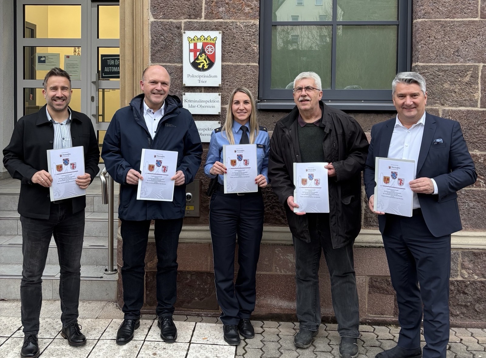 La photo montre les personnes mentionnées. Elles se tiennent devant le bâtiment du commissariat de police et tiennent les documents face à la caméra.