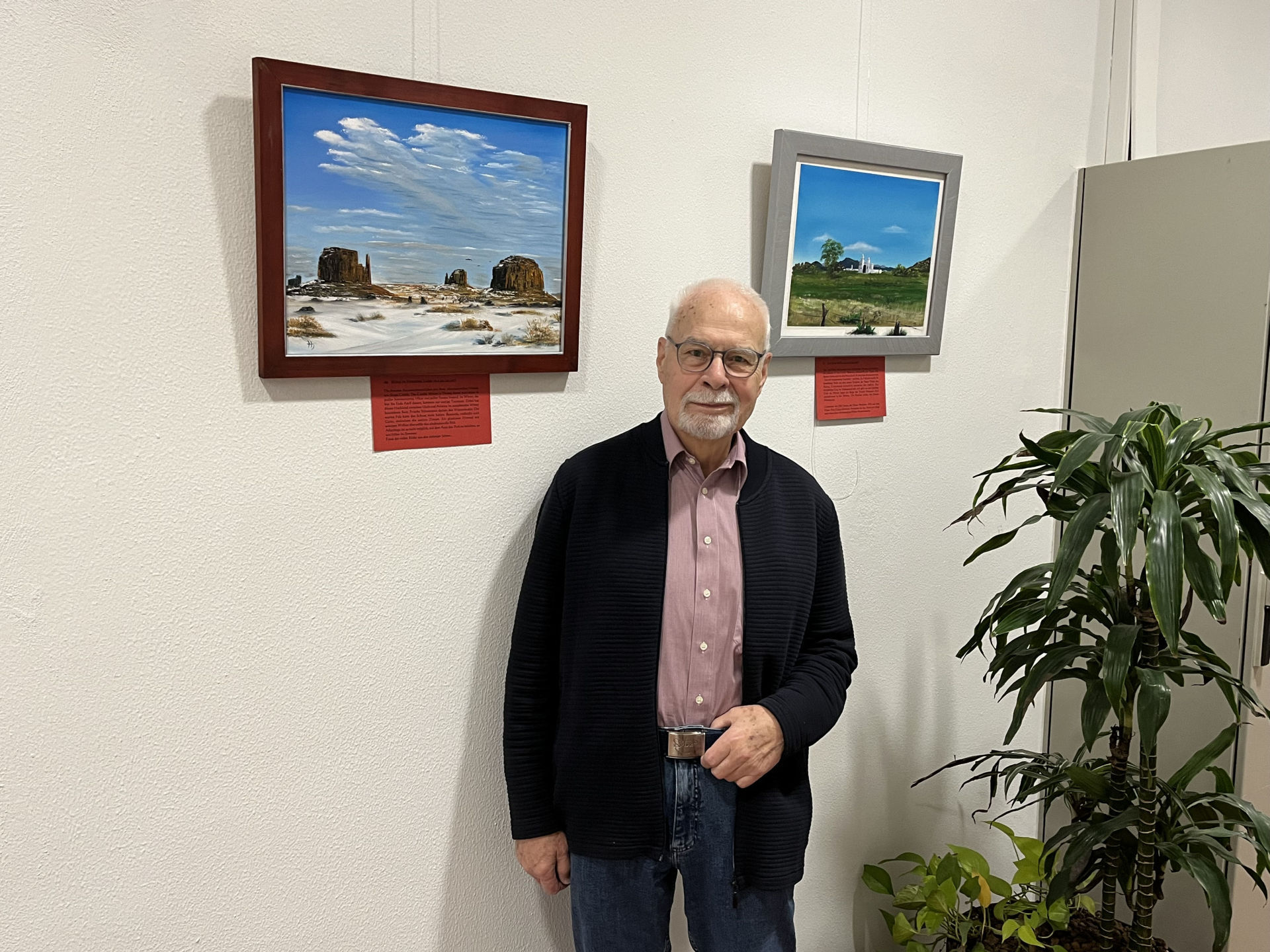 La photo montre le peintre Hartmut Schulz devant deux de ses tableaux dans le foyer. 