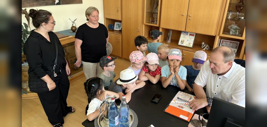 Le maire Frank Frühauf a été très heureux de l'invitation à l'anniversaire de la crèche Enzweiler que les enfants avaient apportée. La photo montre les enfants et les éducateurs, debout autour du bureau du maire Frühauf, qui leur explique quelque chose.