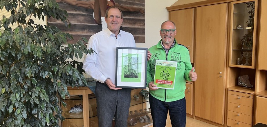 Rainer Hagner remet au maire Frank Frühauf un dessin de la Felsenkirche réalisé par Lennox Düren. La photo montre Rainer et le maire Frank Frühauf remettant le dessin représentant l'église du Rocher.