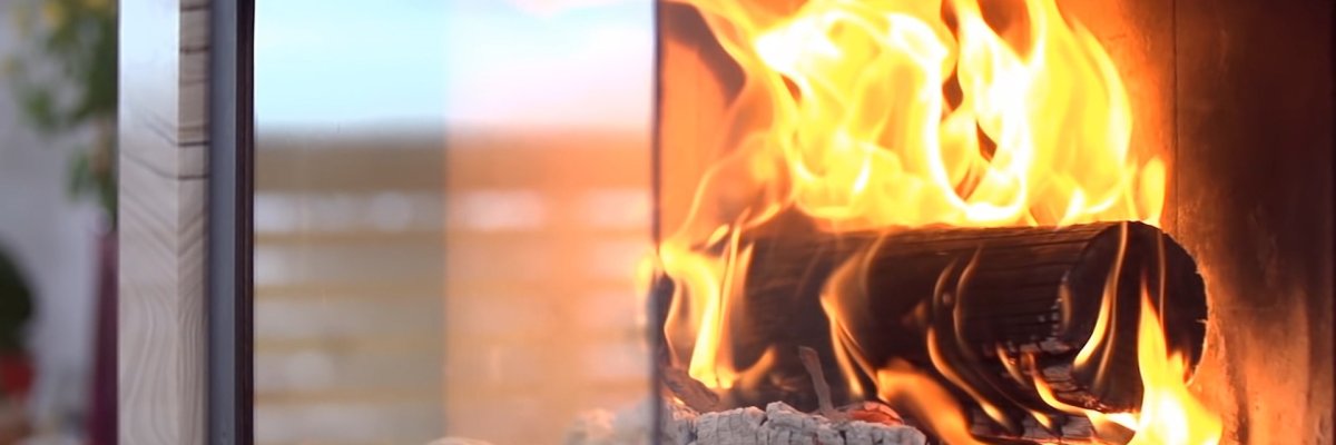 Das Bild zeigt eine Holzfeuer in einem Kaminofen. Die Glasscheibe des Ofens ist halb geöffnet.