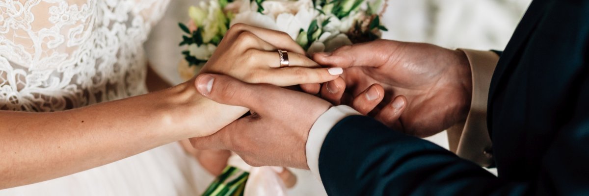 Ein Paar tauscht die Eheringe. Das Foto zeigt in Paar in Hochzeitskleidung, das die Eheringe tauscht.