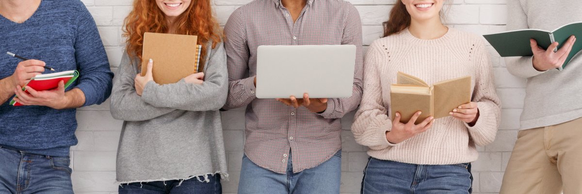 Students with books and laptop standing over light wall Students with books and laptop standing over light wall