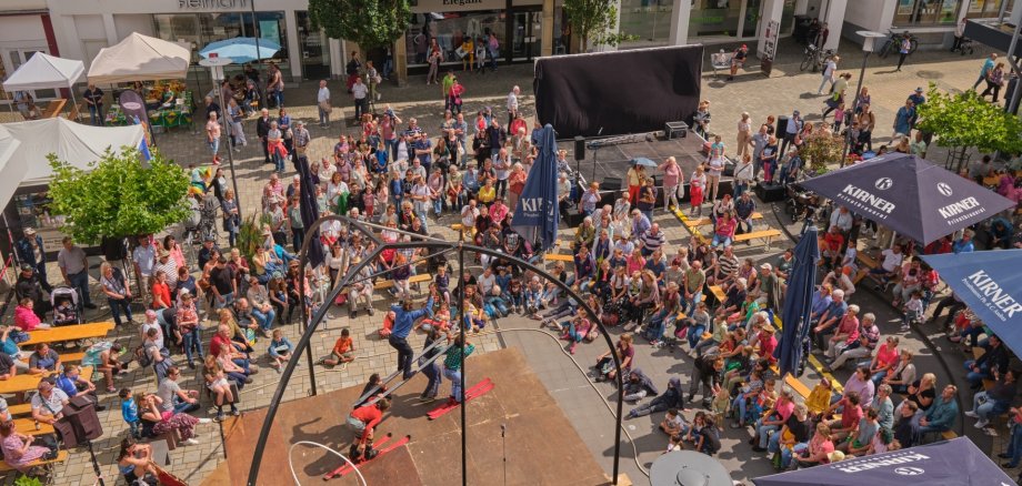 Straßentheater-Festival Das Foto zeigt ein Luftbild von Akrobaten auf Skiern, die vor einer großen Zuschauermenge spielen.