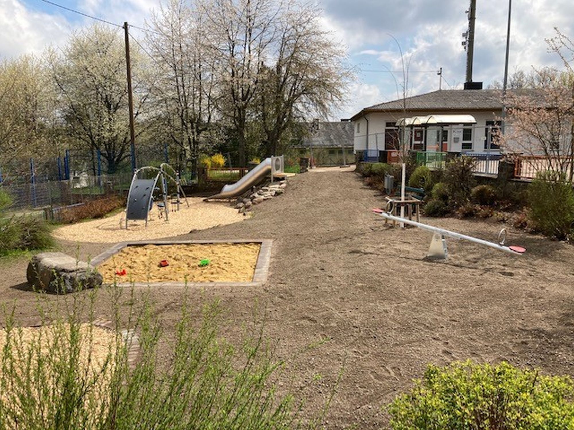Das Foto zeigt einen Blick auf Spieplatz Barbararing mit Sandkasten, Wippe, Rutsche und Klettergerät.