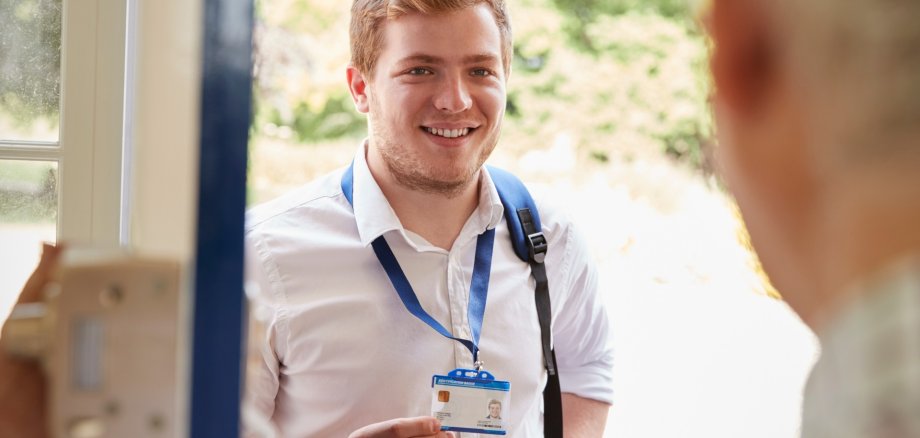 Das Foto zeigt eine Person an der Haustür, die einen Ausweis in der Hand hält und der Person im Haus vorzeigt.