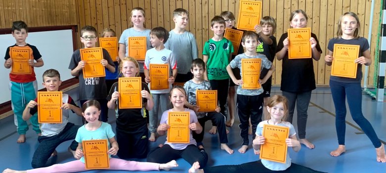 Neben viel Selbstvertrauen erhielten alle Teilnehmer auch eine Urkunde. Das Foto zeigt ein Gruppenbild der Teilnehmer mit ihren Urkunden. Vorne sitzen zwei Mädchen im Spagat.