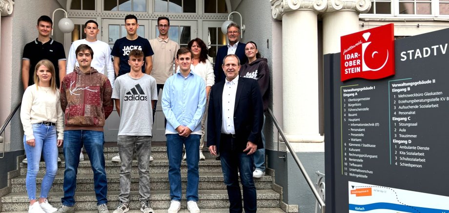 Das Foto zeigt die im Artikel genannten Personen, die in zwei Reihen auf der Außentreppe vor dem Stadthaus stehen. 