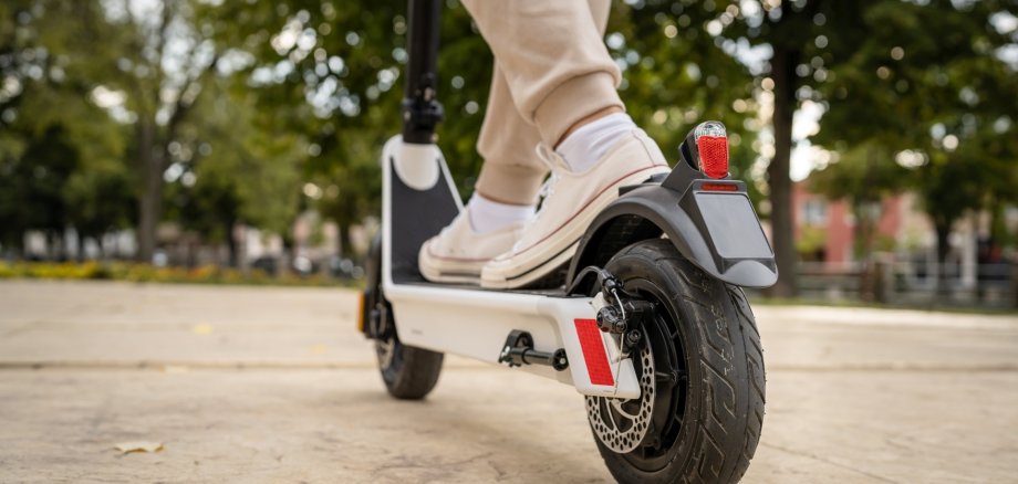 Das Foto zeigt die Füße einer Person, die auf einem E-Scooter stehen.
