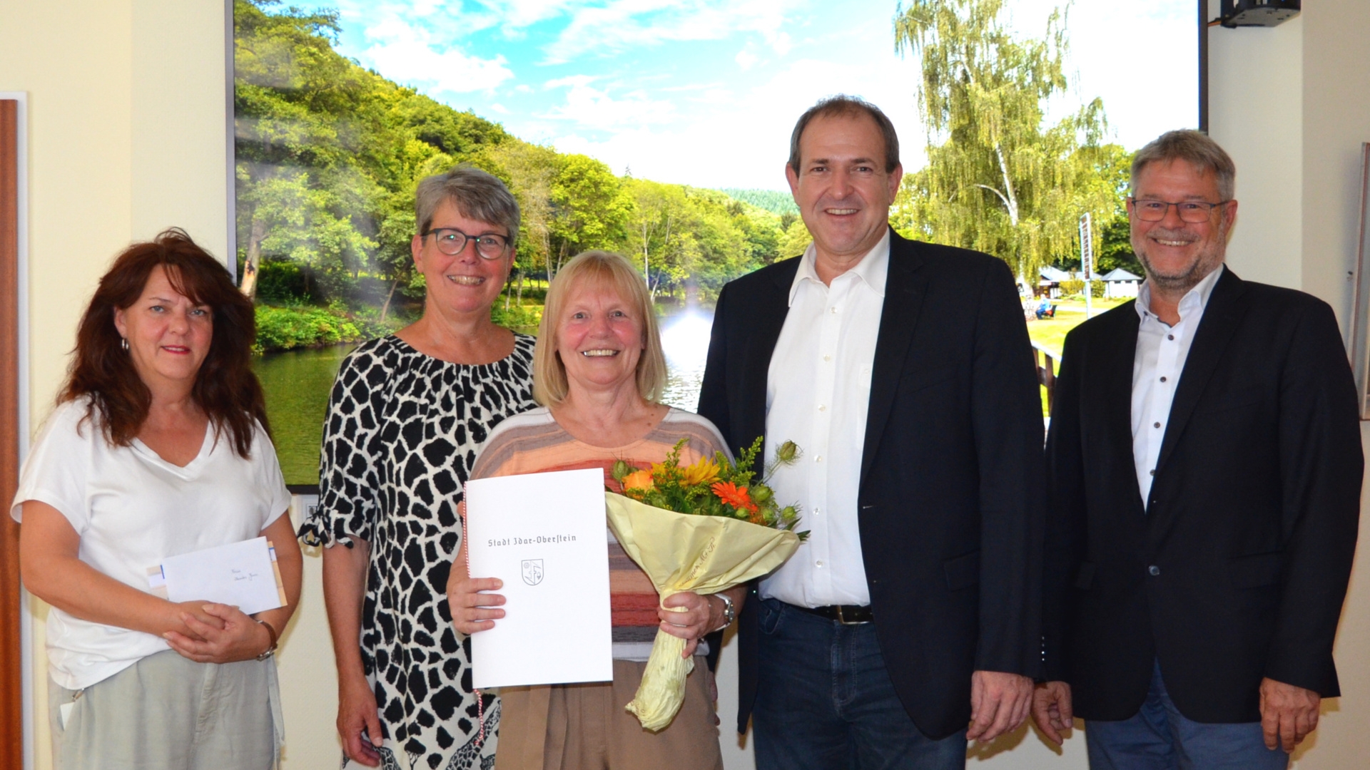 Das Foto zeigt die im Artikel genannten Personen, Monika Gross mit Urkunde und Blumenstrauß.