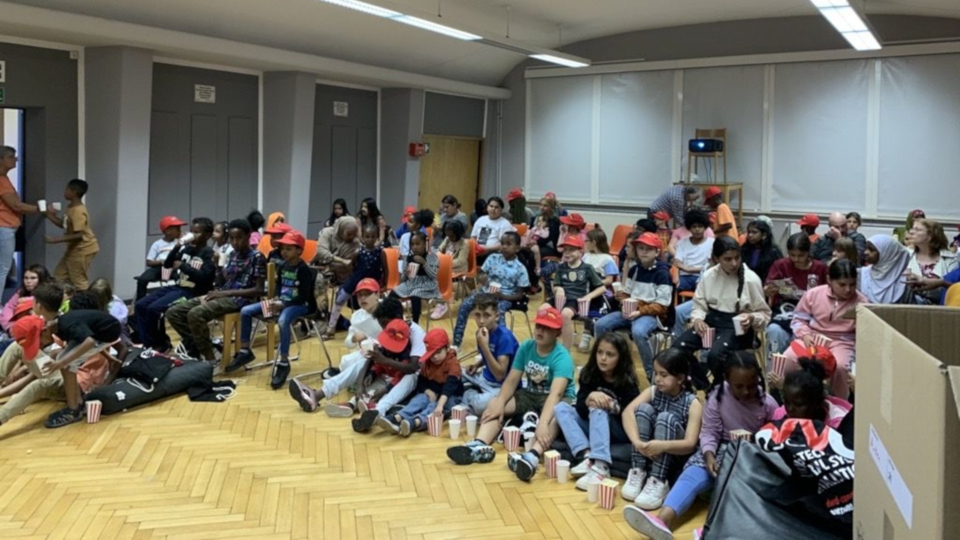 Das Foto zeigt viele Kinder, die im Halbkreis auf dem Boden sitzen und den Film anschauen.