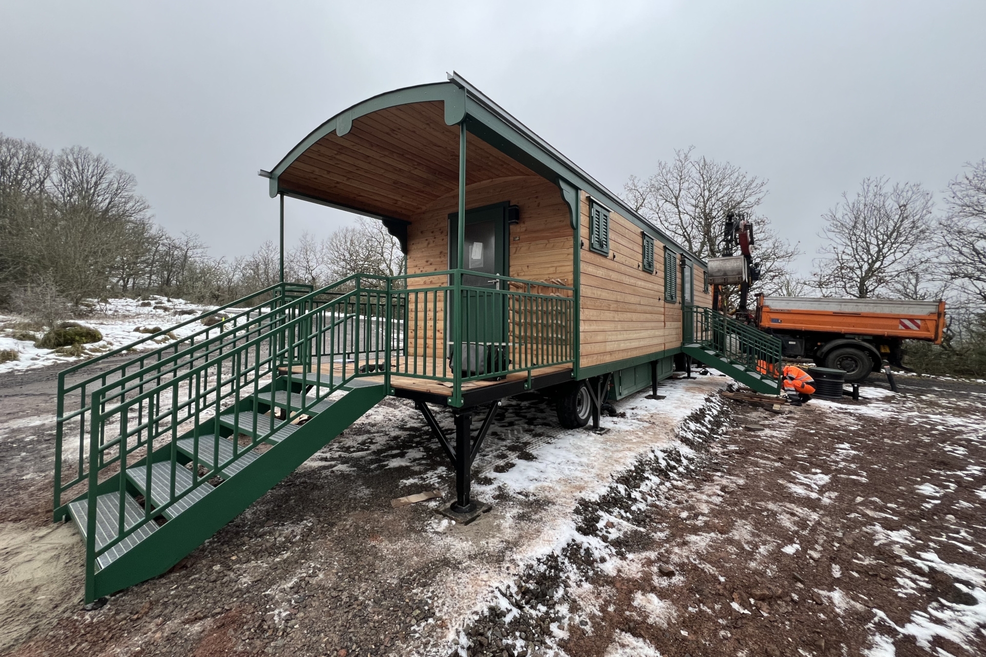Das Foto zeigt den Bauwagen der neuen Waldkita. Arbeiter des Baubetriebshofs sind gerade dabei, eine Treppe zu installieren.