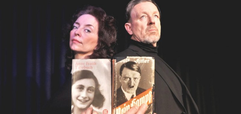 Das Foto zeigt die beiden Schauspieler, die Rücken an Rücken vor einem schwarzen Bühnenvorhang stehen. Marianne Blum hält das Tagebuch der Anne Frank, Thomas Linke Adolf Hitlers Mein Kampf.