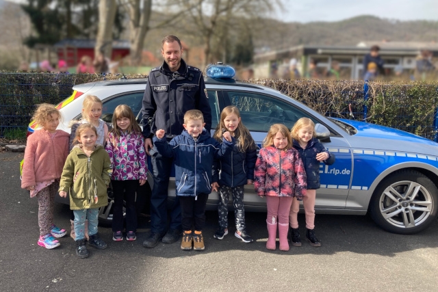 Das Foto zeigt mehrere Kinder, die mit dem Polizisten Pascal Stamm vor einem Polizeiauto stehen.