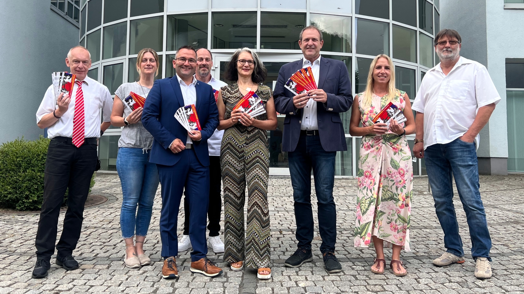 Das Foto zeigt mehrere Personen, die mit Flyern des Theatersommers vor dem Firmengebäude der OIE AG stehen. 