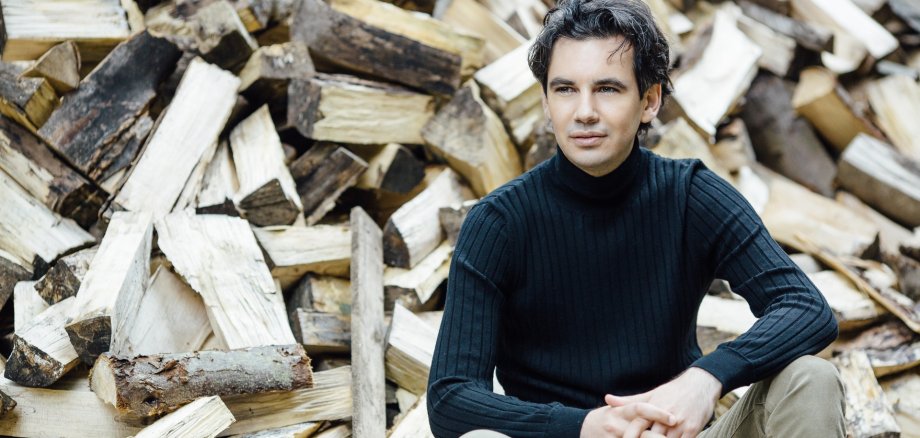 Das Foto zeigt Martin Stadtfeld vor einem Holzstapel.