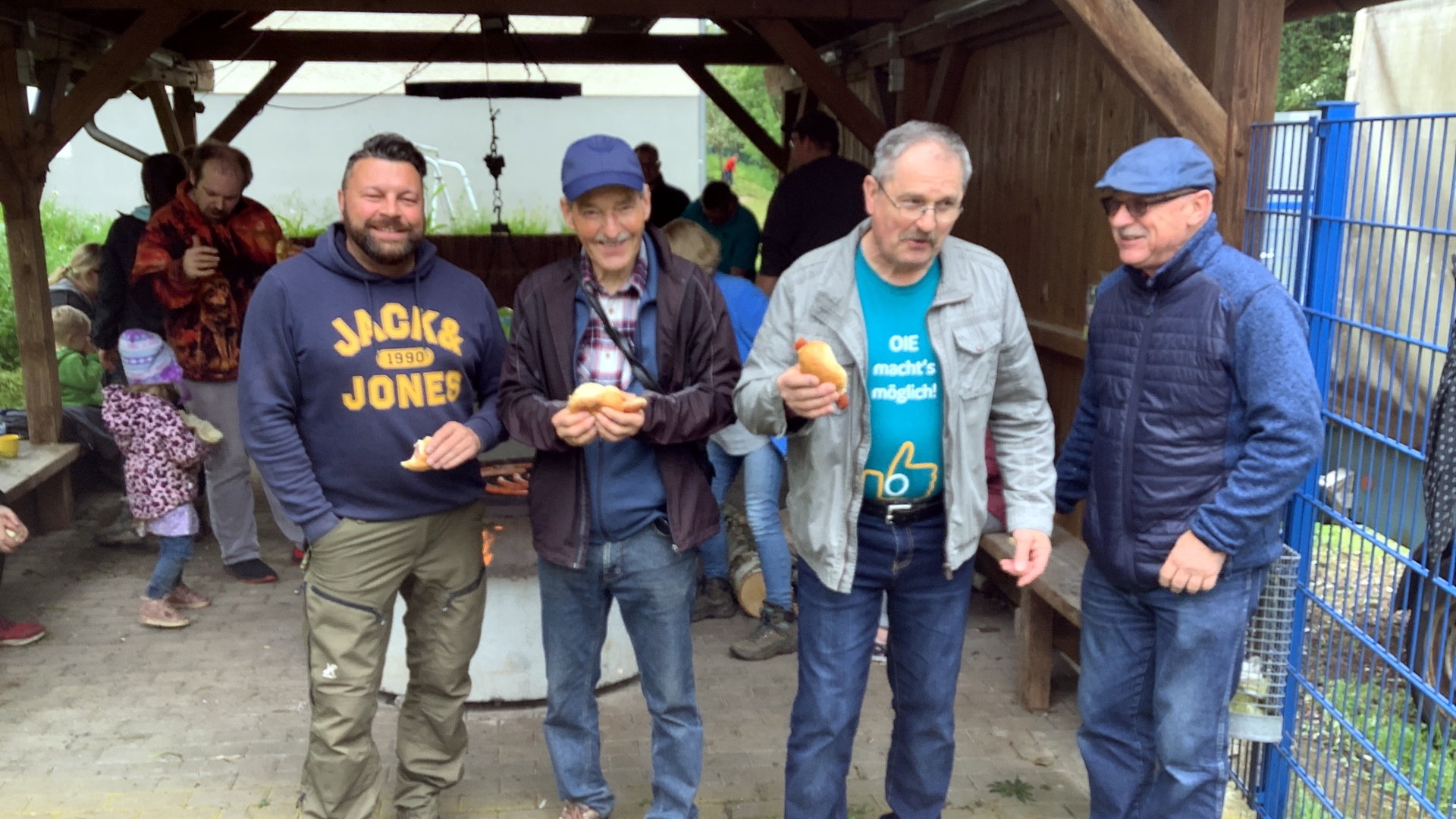 Das Foto zeigt vier Mitglieder der Offenen Gruppe Nahbollenbach, die mit Würstchen vor dem Grillrost stehen.