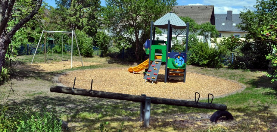 Das Foto zeigt Teile der Spielgeräte auf dem Spielplatz Wiesendellstraße. Im Vordergrund ist eine Wippe, im Hintergrund sind die neue Doppelschaukel und das neue zentrale Spielgerät zu sehen.