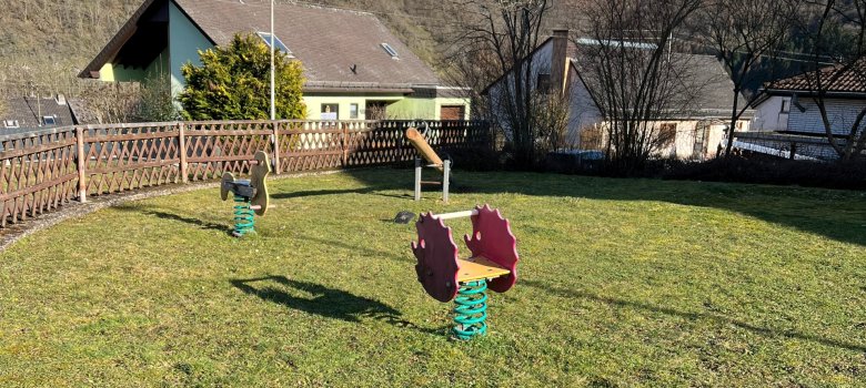 Das Foto zeigt den bisherigen Spielplatz, eine Wiese mit zwei Federspielgeräten und eine Wippe.