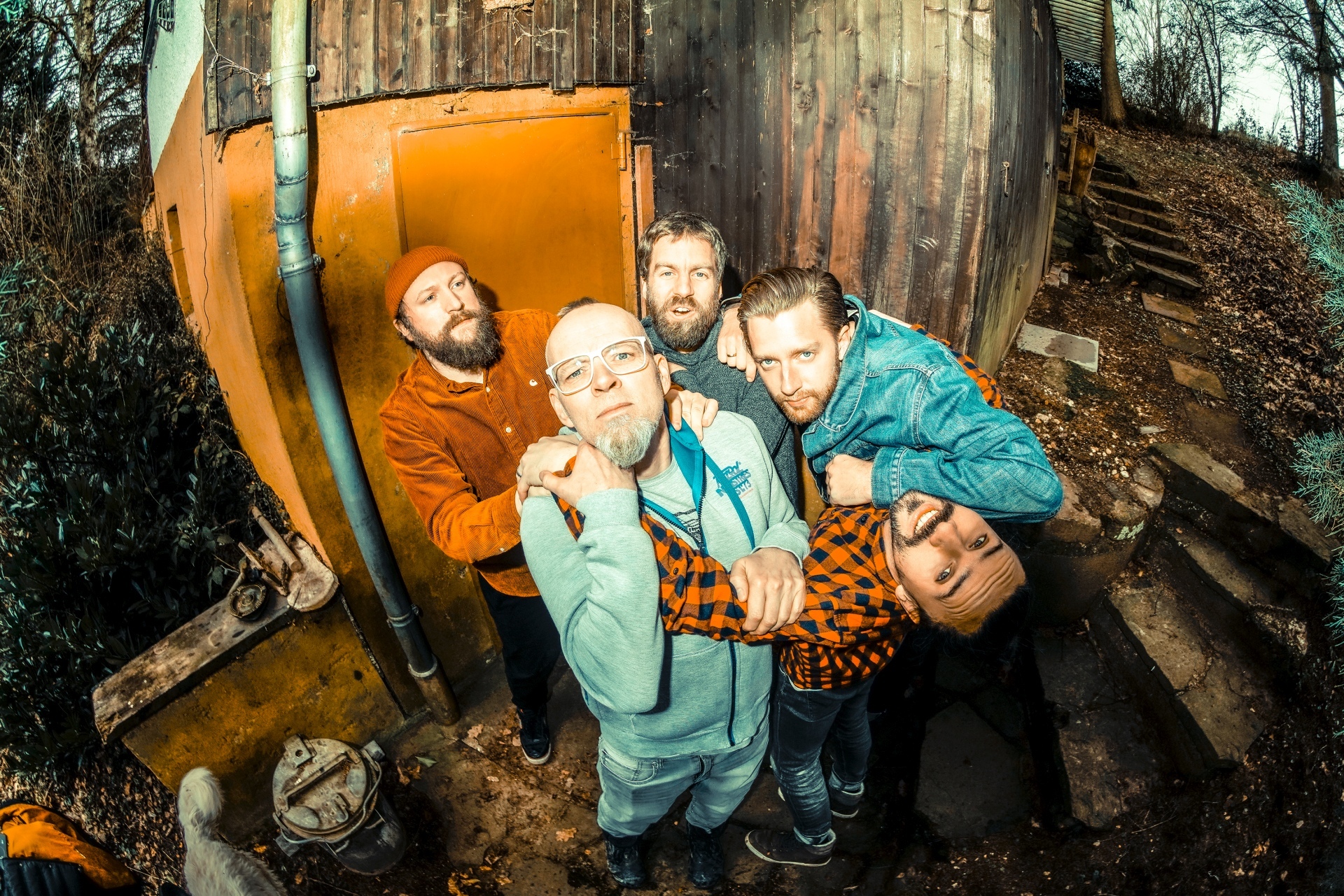 Das Foto zeigt Thomas D und die Mitglieder der Band The KBCS vor einer Hütte im Wald.