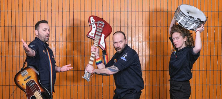 Das Foto zeigt die drei Musiker der Band Raketen Erna mit ihren Instrumenten vor einer Fliesenwand.