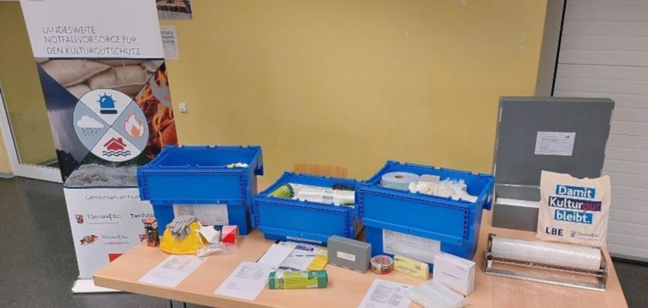 Das Foto zeigt einen Tisch, auf dem die drei Boxen des Notfallsets stehen. Vor den Boxen ist deren jeweiliger Inhalt ausgebreitet.