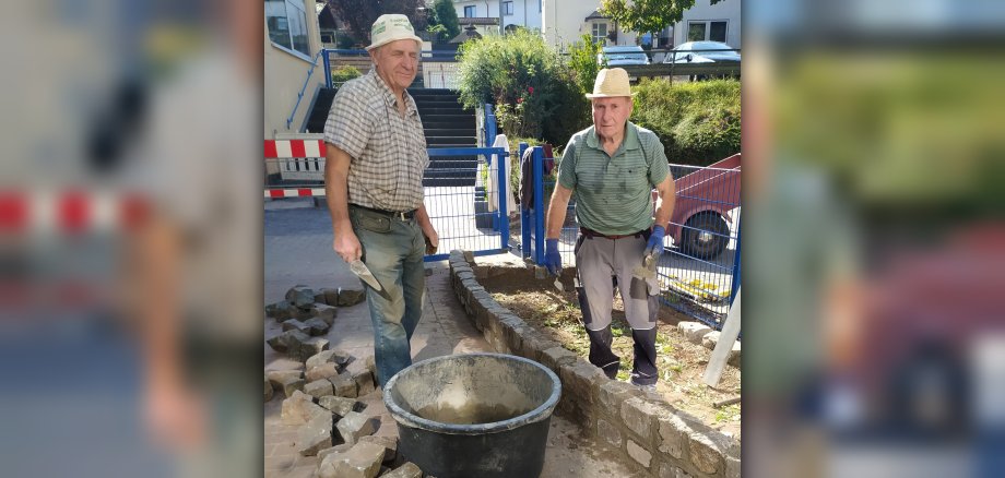 Das Foto zeigt zwei Mitglieder der Offenen Gruppe in Arbeitsbekleidung. Sie stehen an der Mauer, die sie gerade errichten.