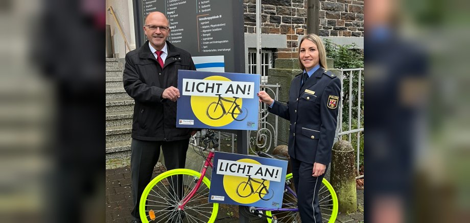 Das Foto zeigt Bürgermeister Marx und Polizeirätin Short. Sie stehen mit einem der angesprühten Räder vor dem Rathaus und halten gemeinsam ein Schilde mit der Aufschrift "Licht an!"