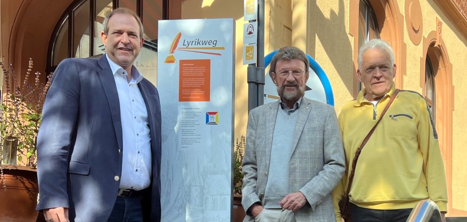 Das Foto zeigt die genannten Personen. OB Frühauf steht links von der Hinweis-Stele des Lyrikweges am Aufgang zur Felsenkriche. Wolfgang Hey und Joachim Schroetter rechts davon.