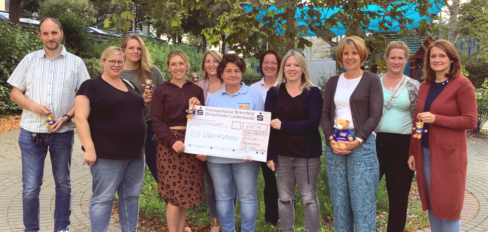 Das Foto zeigt neun Personen, die nebeneinander in einer Reihe stehen. Drei Frauen in der Mitte halten einen großen Spendenscheck über 600 Euro.