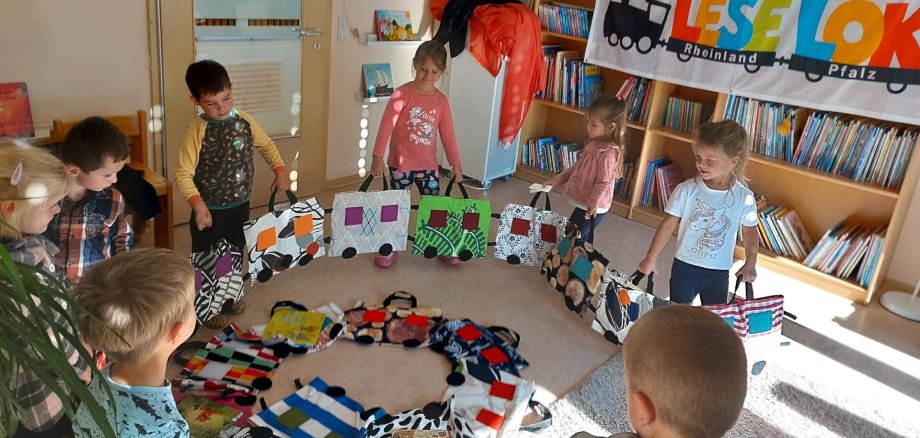 Das Foto zeigt einen Blick in das Lesezimmer der Kita. Einige Kinder knien im Kreis um den Zug und halten die jedes zwei Waggons in den Händen. Am Bücherregal im Hintergrund hängt ein Banner mit der Aufschrift "Lese-Lok".
