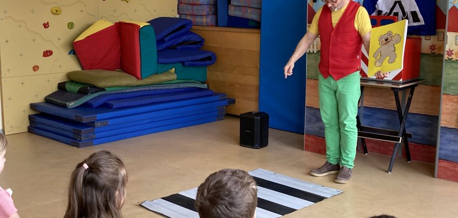 Das Bild zeigt den Zauberer Robert, der vor einem stilisierten Zebrastreifen steht und den Kindern der Kita erklärt, was zu tun ist. 