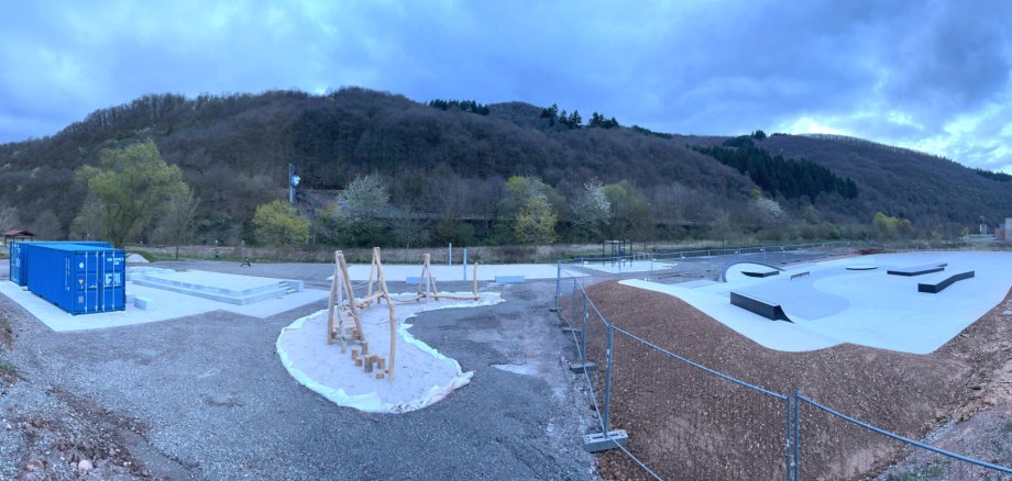 Das Foto zeigt eine Panoramaaufnahme der Anlage mit von links Toiletten- und Aufenthaltscontainer, Bühne, Inklusionsschaukel, Beachvolleyballfeld, Mehrzweckspielfeld und Skateranlage.