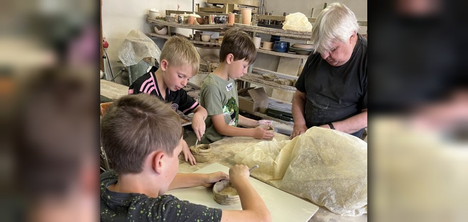 Das Foto zeigt die Kinder gemeinsam mit Töpfermeister Manfred Weigel beim töpfern.