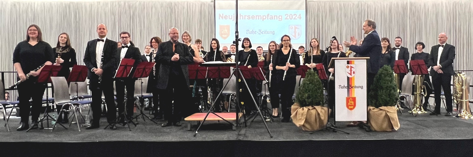 Das Foto zeigt einen Blick auf die Bühne des Neujahrsempfangs. Die Mitglieder des SBO stehen auf der Bühne, Oberbürgermeister Frühauf steht am Rednerpult, hat sich dem Orchester zugewandt und applaudiert.