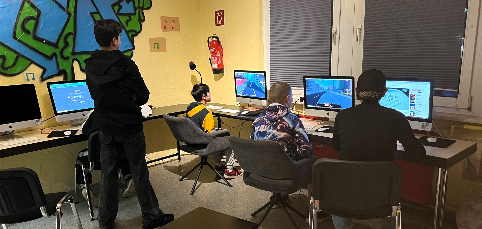 Das Foto zeig einen Blick in den Jugendtreff. Drei Jugendliche sitzen an Tischen vor Computerbildschirmen. Einer steht dahinter un beobachtet die anderen.