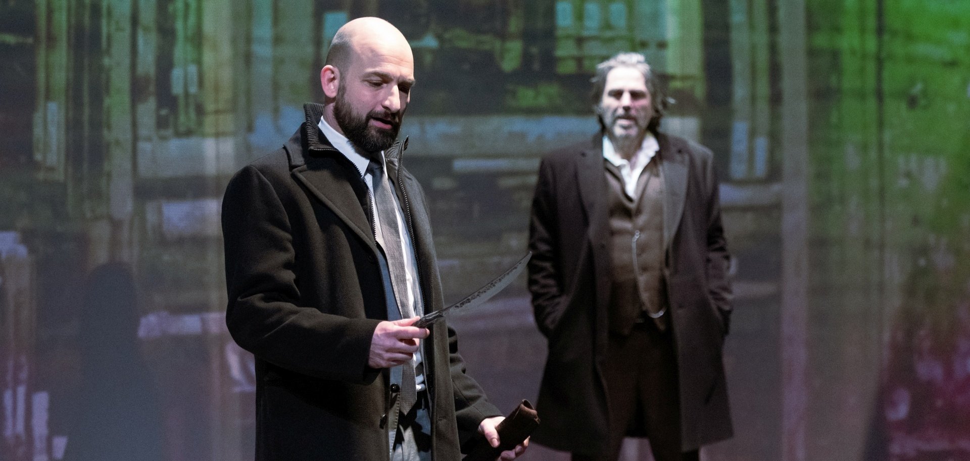 Das Foto zeigt zwei Schauspieler auf der Bühne. Einer hält ein Messer in der Hand.