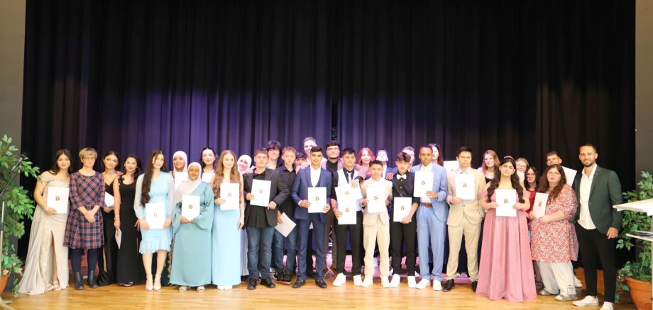 Das Foto zeigt die Schülerinnen und Schüler bei der Zeugnisübergabe auf der Bühne der Göttenbach-Aula. 