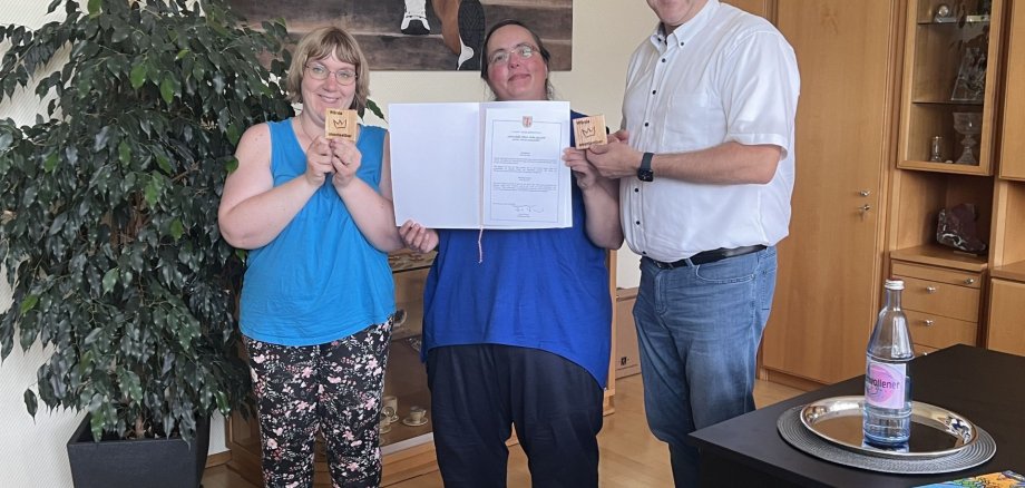Das Foto zeigt Oberbürgermeister Frühauf mit zwei Beschäftigten der Nahe-Hunsrück-Werkstätten, die ihm "Würde-Täfelchen" überreichen. 