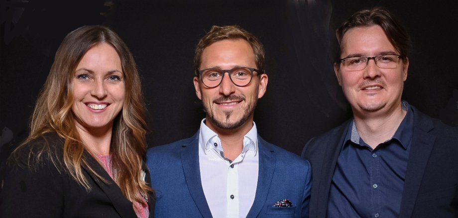 Das Foto zeigt die drei Bandmitglieder, die nebeneinander stehen und in die Kamera schauen.
