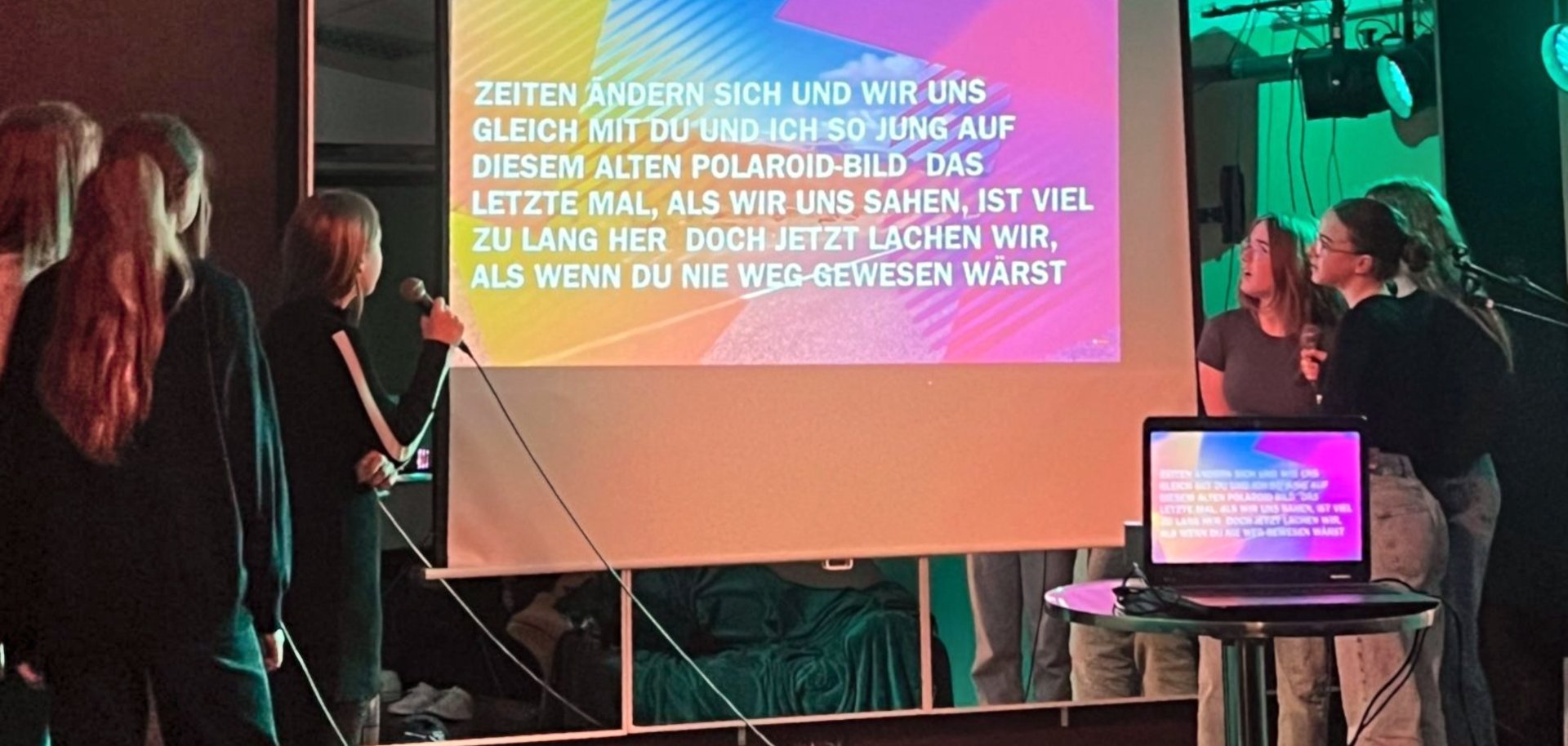 Das Foto zeigt mehrere Jugendliche, die vor einer Leinwand stehen. Auf der Leinwand ist ein Liedtext zu sehen, die Jugendlichen singen dazu Karaoke.