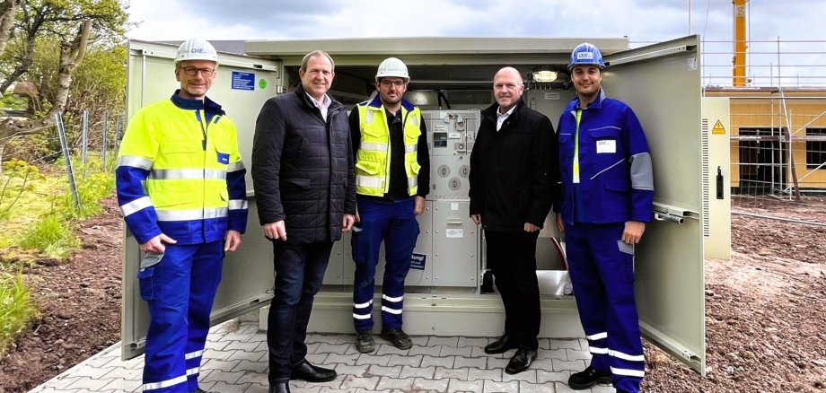 Das Foto zeigt die genannten Personen. Sie stehen nebeneinander vor einer geöffneten Ortsnetzstation und blicken in die Kamera.