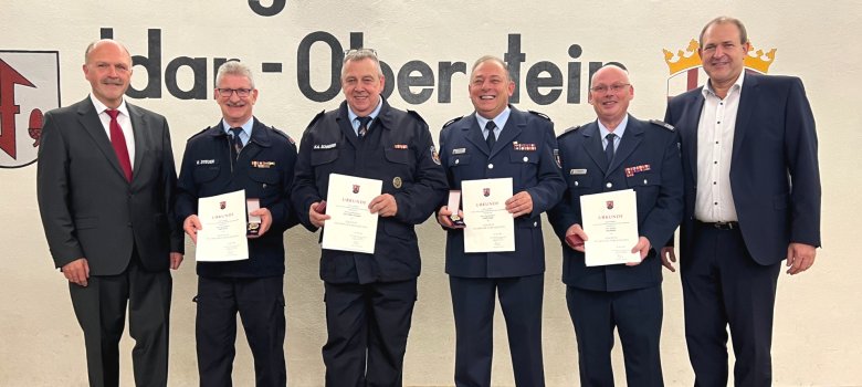 Das Foto zeigt die Geehrten mit Gratulanten. Sie stehen nebeneinander auf der Bühne und blicken in die Kamera.