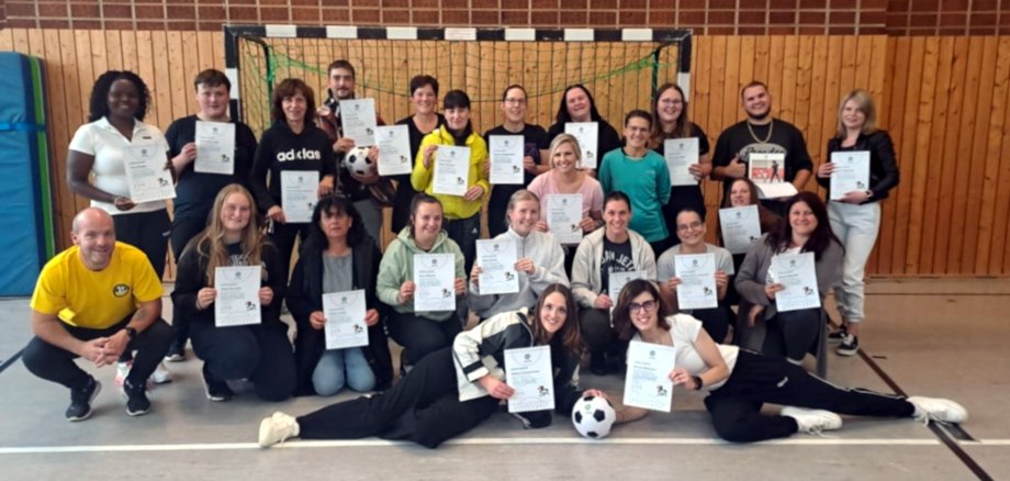 Das Foto zeigt die Teilnehmer und den Dozent der Fortbildung. Sie befinden sich in drei Reihen in einer Turnhalle. Die hintere Reihe steht, die mittlere Reihe kniet und davor liegen noch zwei Personen.